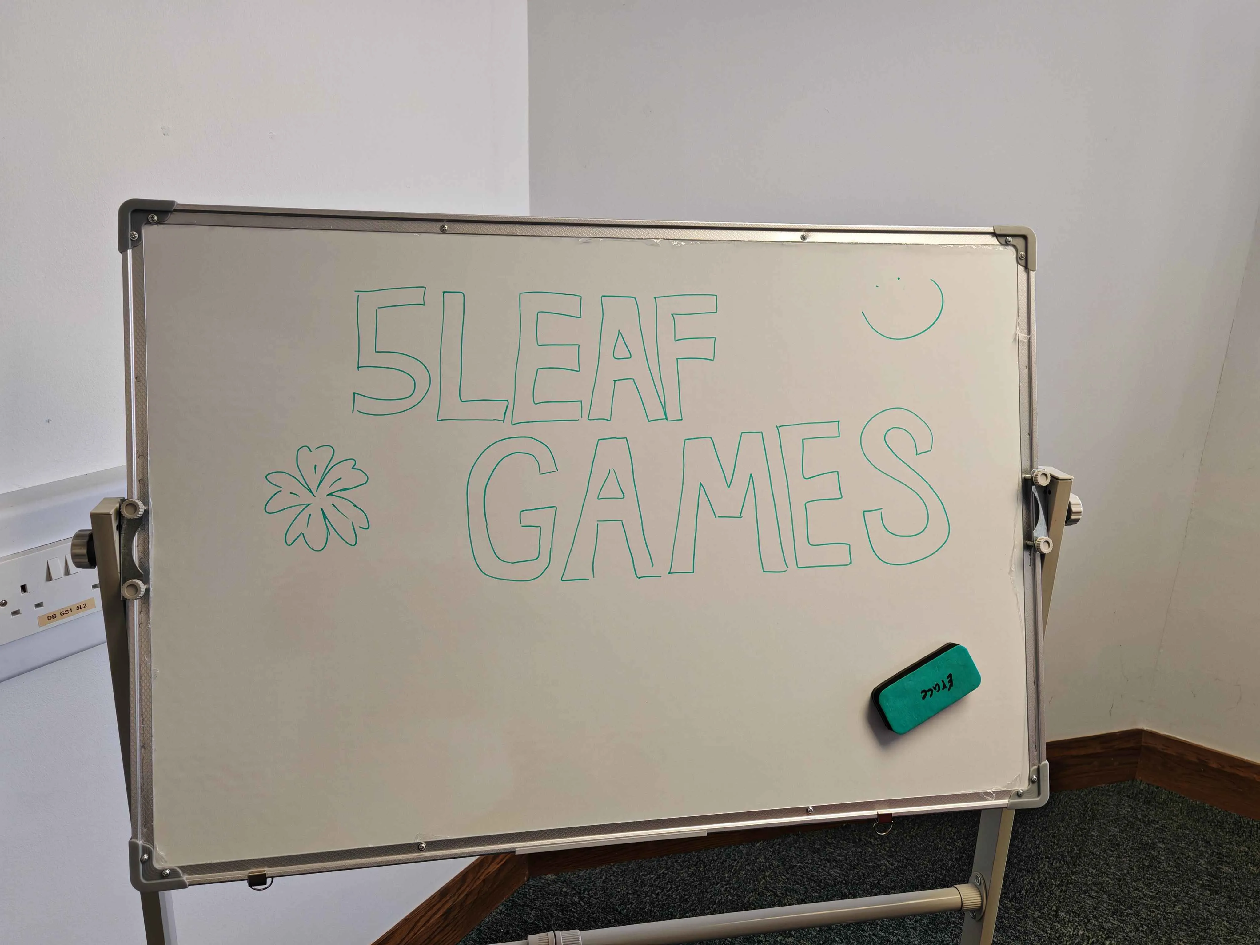 The office whiteboard, it reads "5Leaf Games" in thick block text, and it has a little 5-leaf clover and a smiley face in opposite corners
